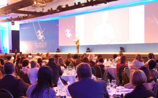 Orientadores de Kumon en un evento presencial, y en el escenario, un colaborador de Kumon dando una conferencia